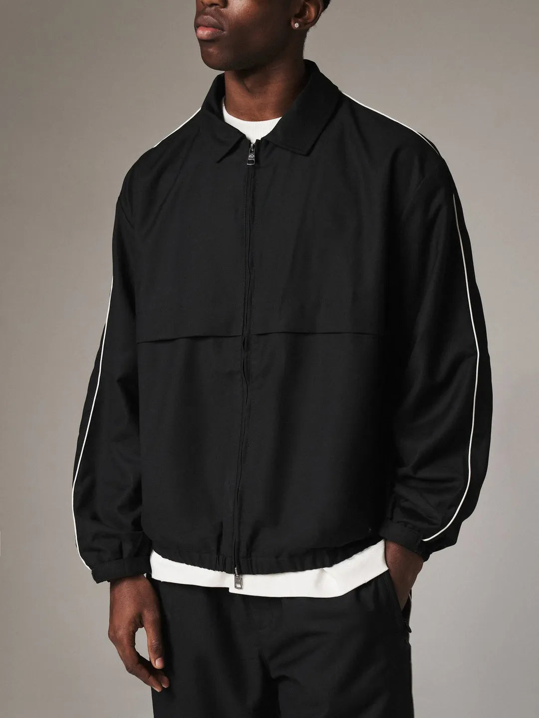 Person wearing a black jacket with white accents on a gray background