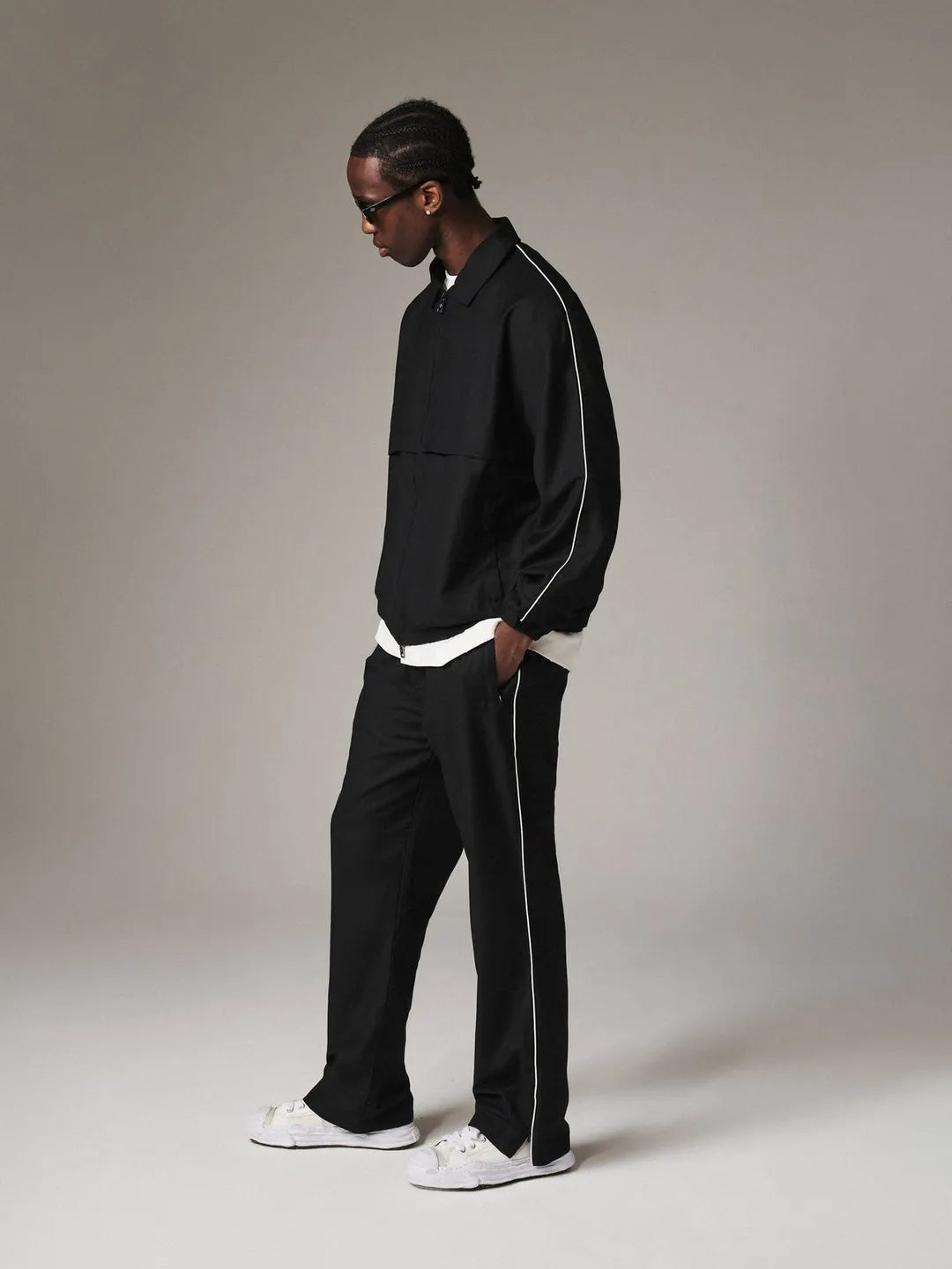 Man wearing a black tracksuit with white stripes on a plain background