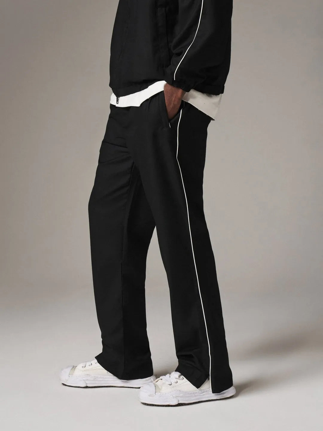Person wearing black pants with white piping and a black jacket on a plain background
