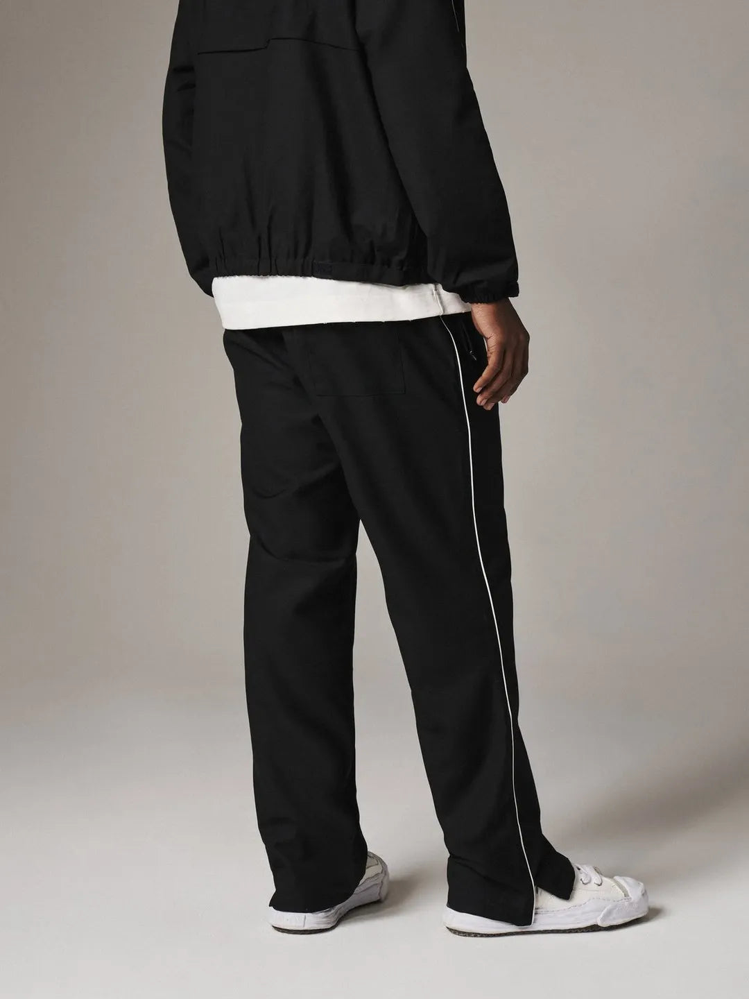 Person wearing black pants with a white stripe on a plain background