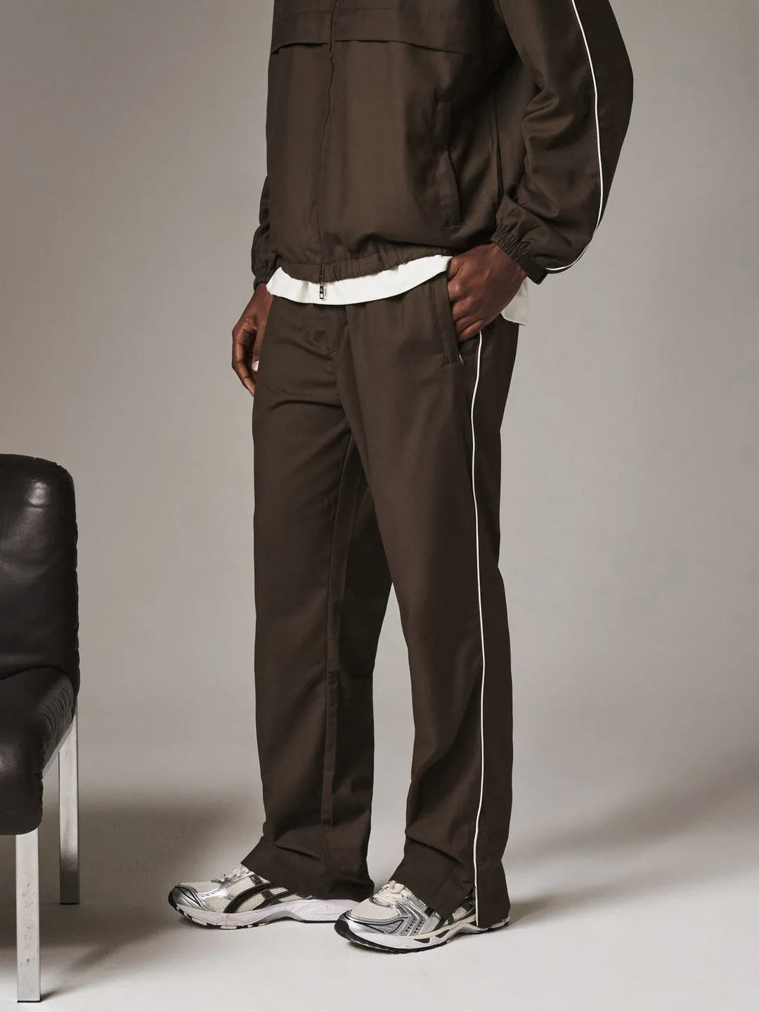 Person wearing a brown tracksuit with white stripes on a plain background