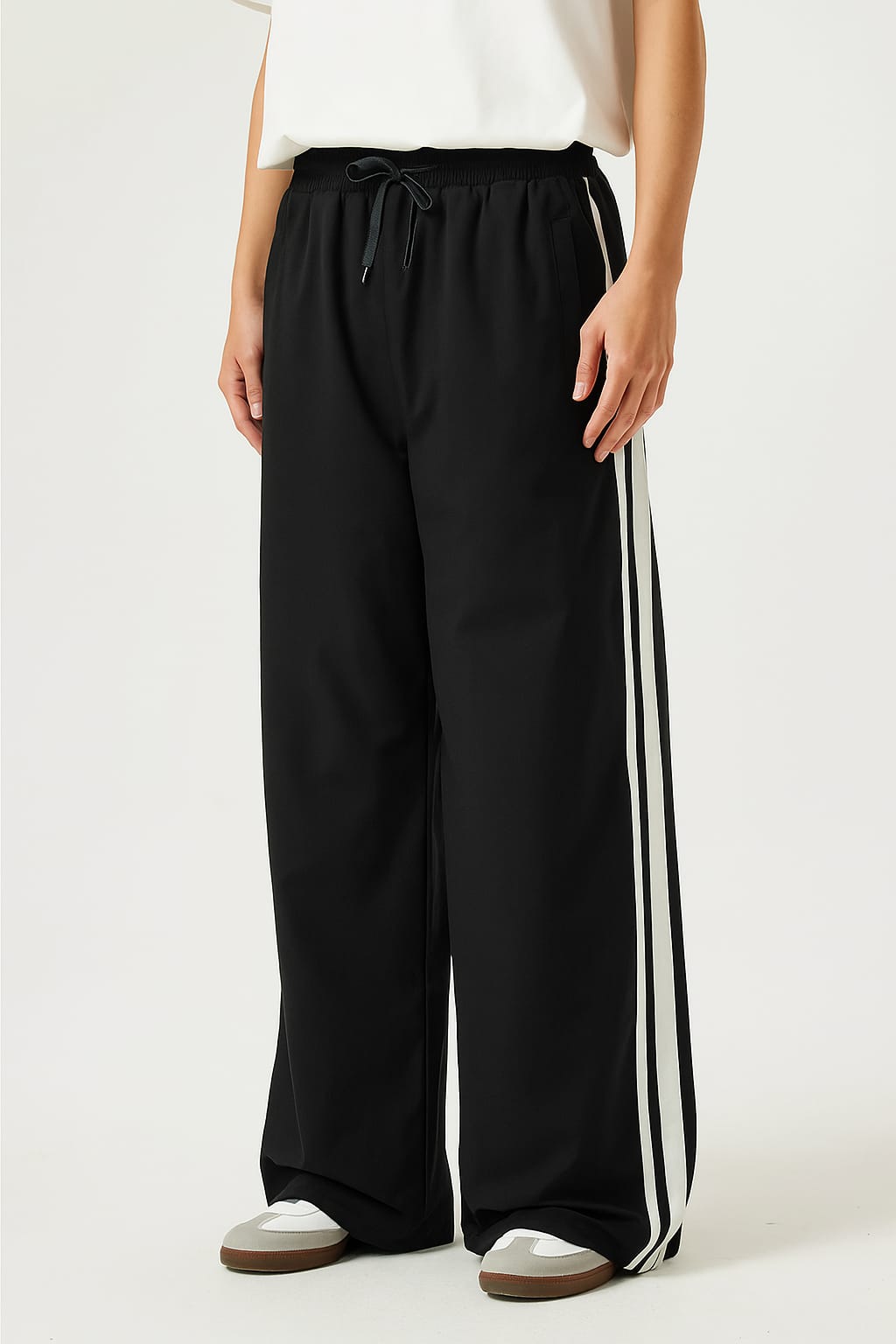 A person wearing a black tracksuit with white stripes on a white background