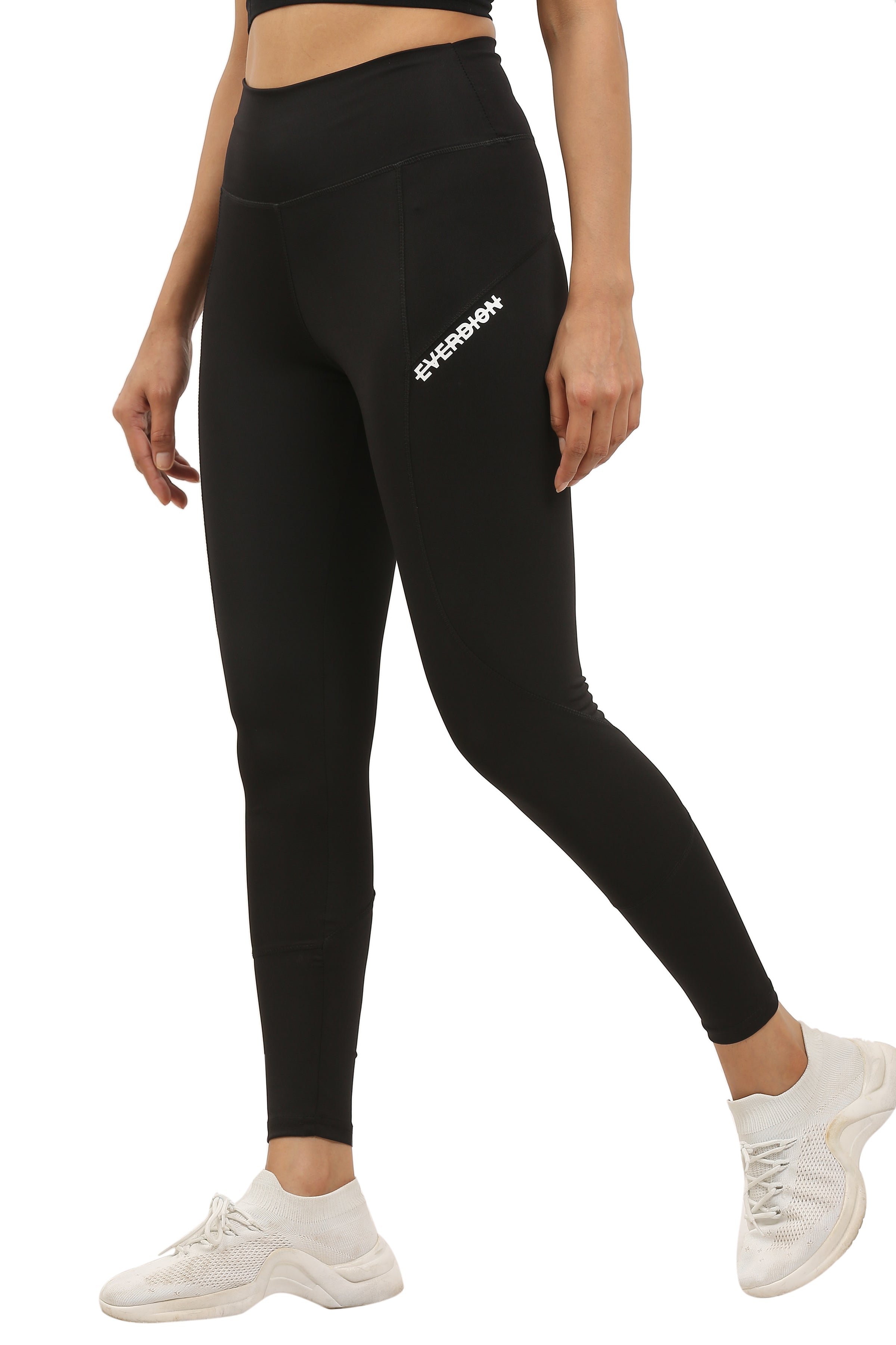 A model wearing high-rise black gym tights and white sneakers, standing on one leg with the other foot raised.