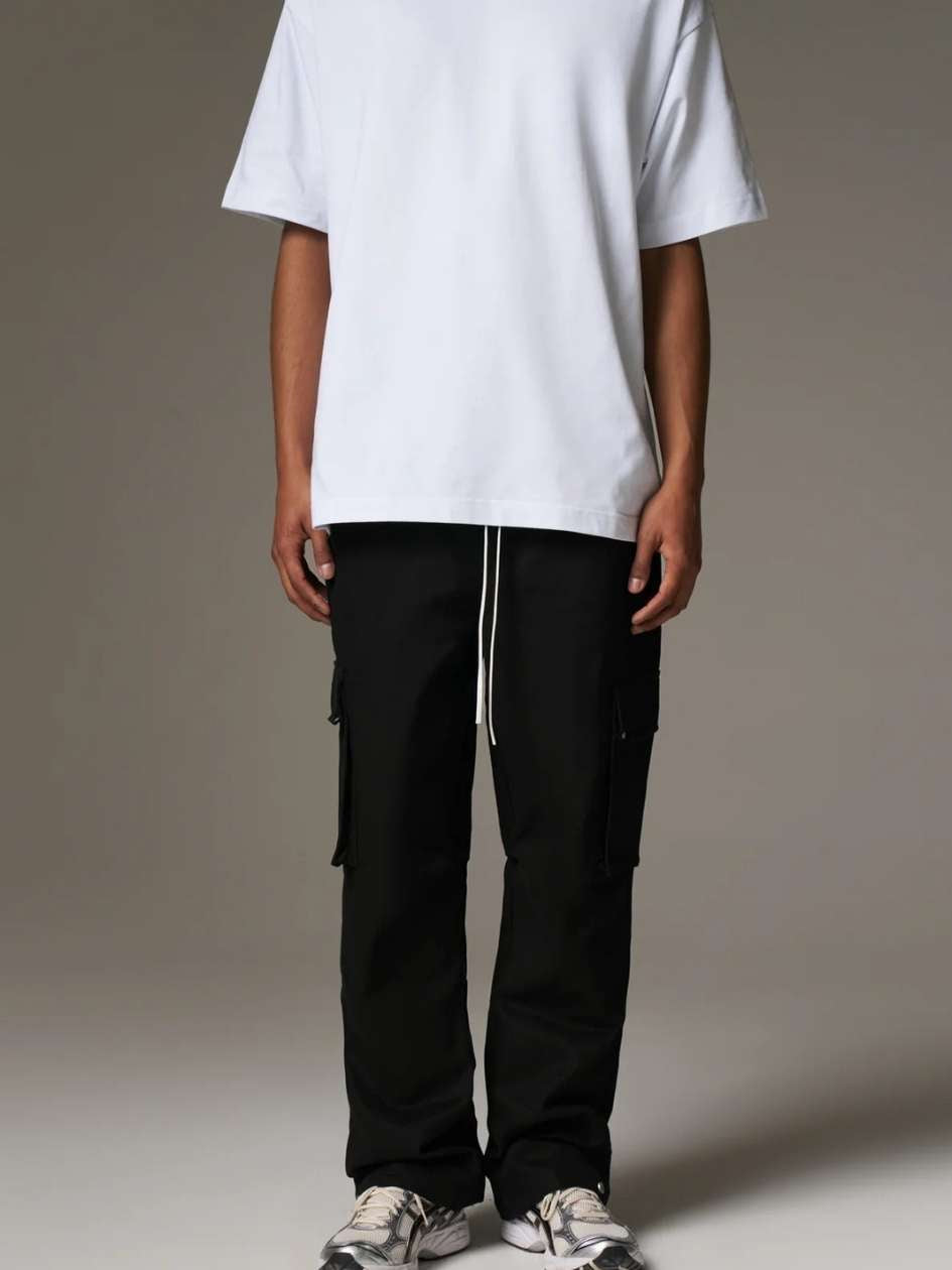 Person wearing a white oversized t-shirt and black cargo pants on a plain background