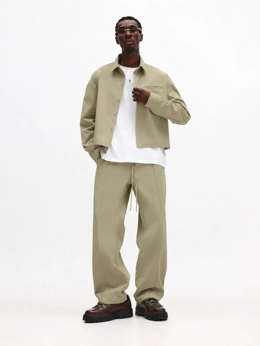 Man wearing a beige jacket and pants with a white shirt on a white background