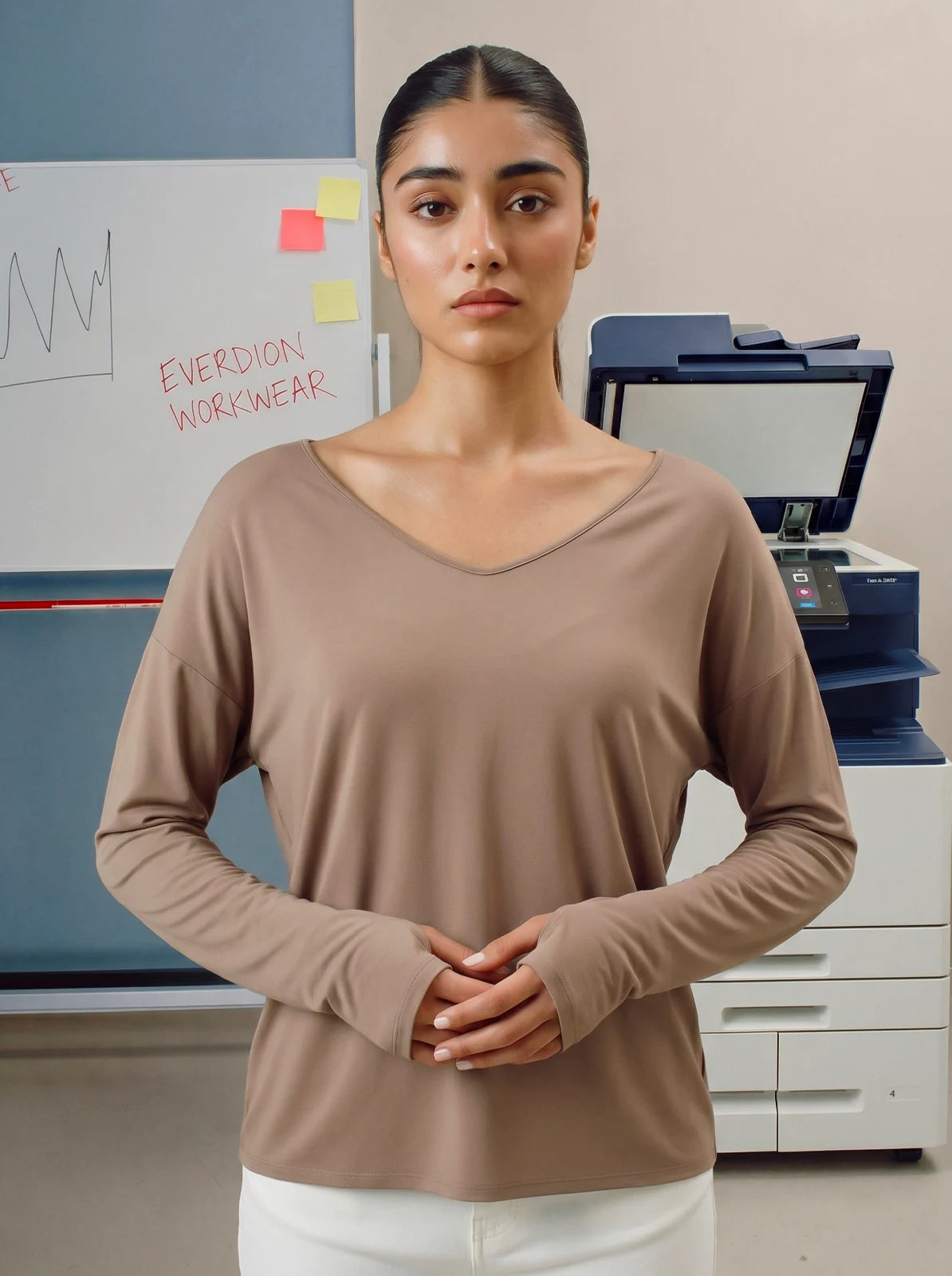 Woman wearing a brown long-sleeve top standing in an office setting with a printer and whiteboard in the background.