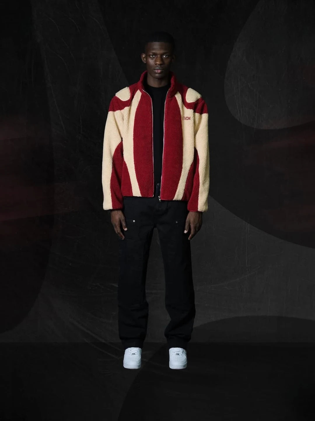 Person wearing a red and beige jacket with a dark background
