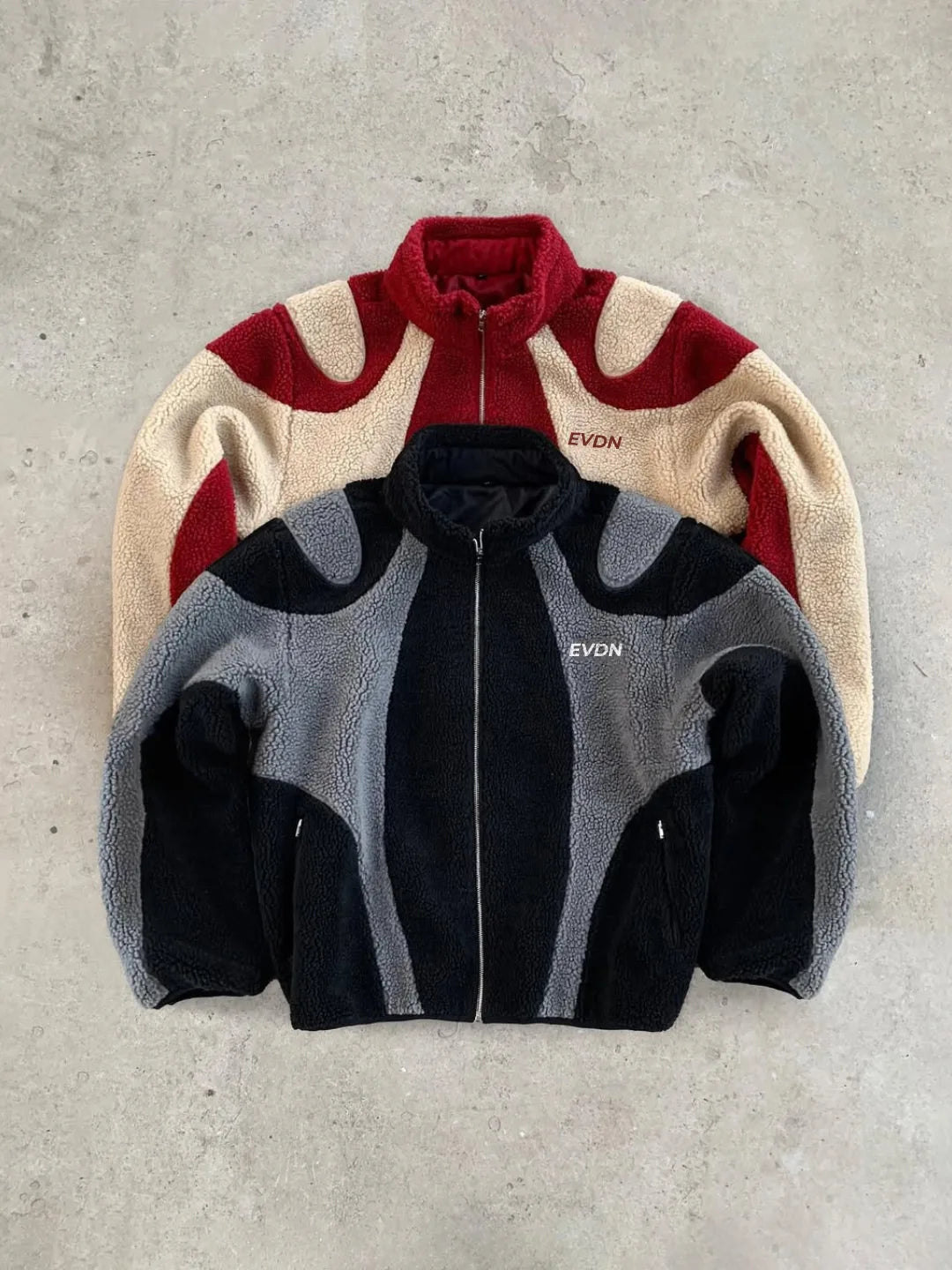 Two jackets, one red and beige, one gray and black, on a concrete surface.
