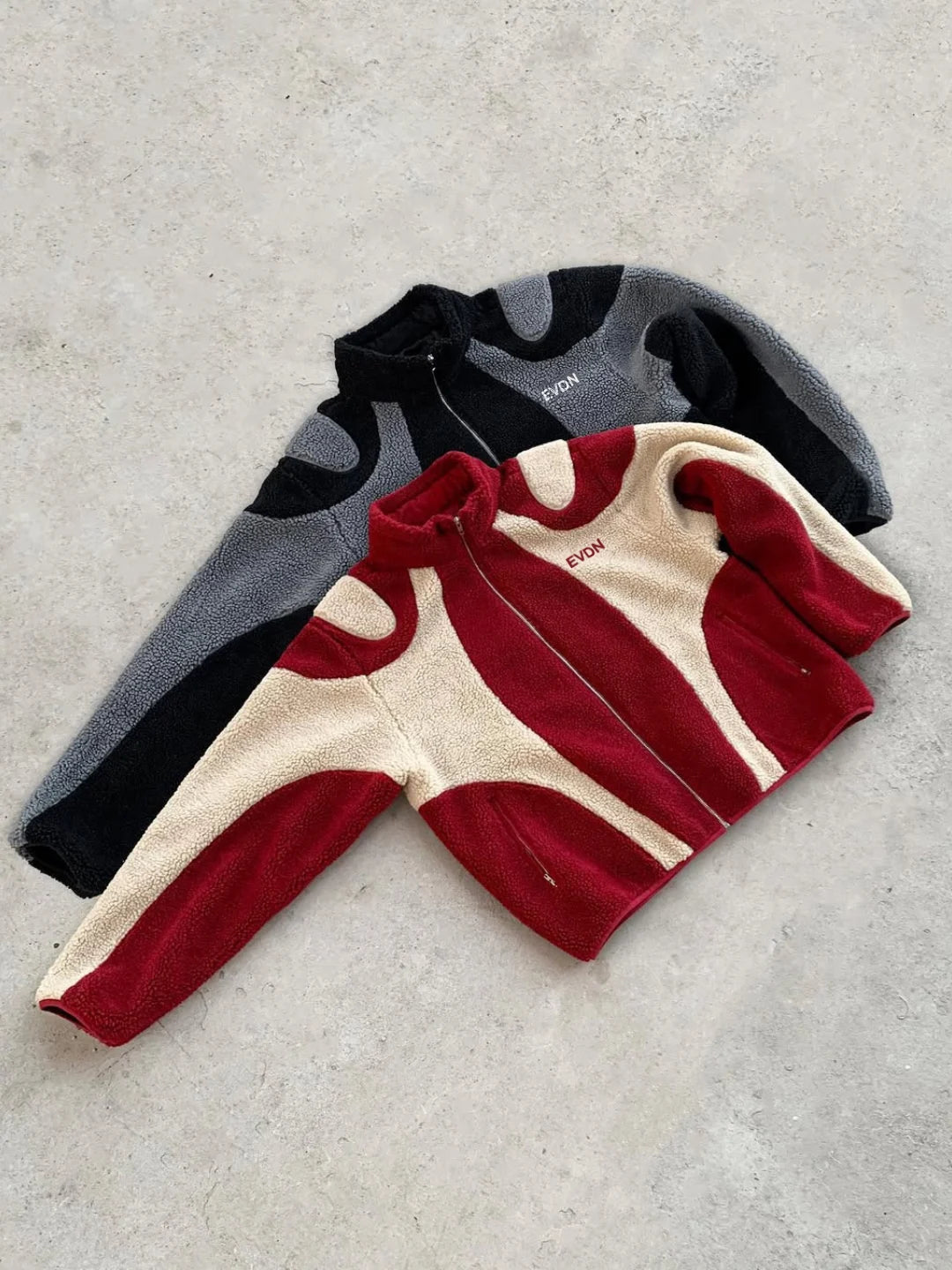 Three children's sweaters in red, gray, and black on a light gray surface.