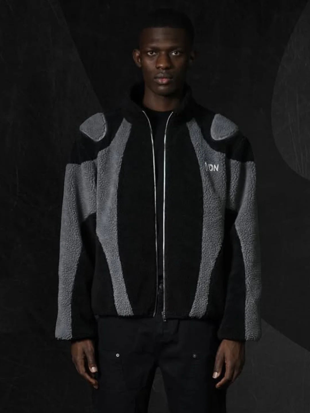 Person wearing a black and gray patterned jacket with 'EVDN' branding on a dark background