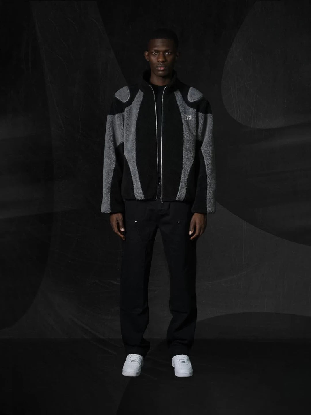 Person wearing a black and gray jacket with a dark background