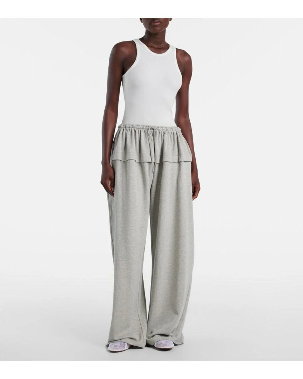 Person wearing a white sleeveless top and grey wide-leg pants on a white background