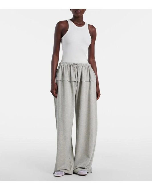Person wearing a white sleeveless top and grey wide-leg pants on a white background