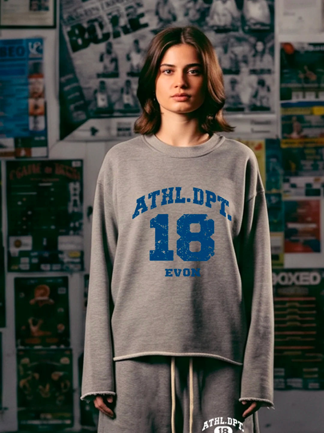 A woman wearing a heather grey cropped sweatshirt with blue collegiate-style text reading 'ATHL. DPT.
