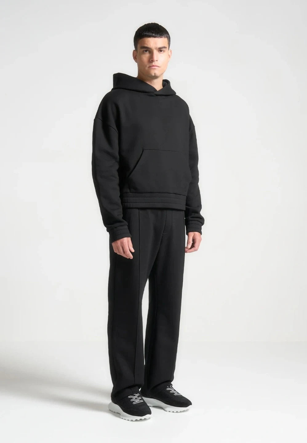 Person wearing a black hoodie and pants on a white background
