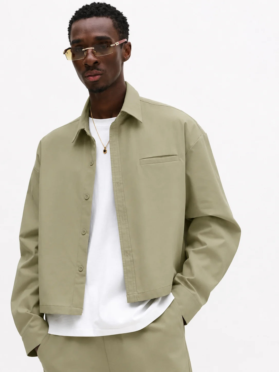Man wearing a beige shirt over a white t-shirt on a plain background
