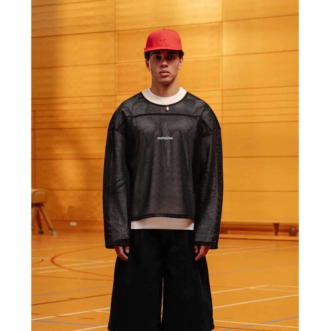 Person wearing a black mesh sports outfit with a red cap in an indoor basketball court.