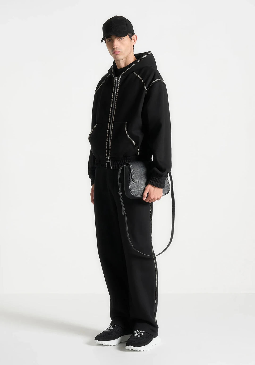 Person wearing a black outfit with a matching bag on a white background