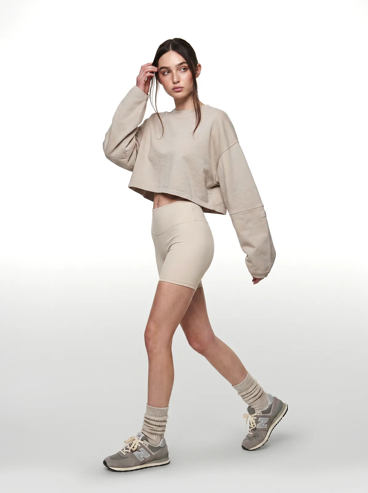 Woman wearing a beige cropped t-shirt, shorts, and sneakers on a white background