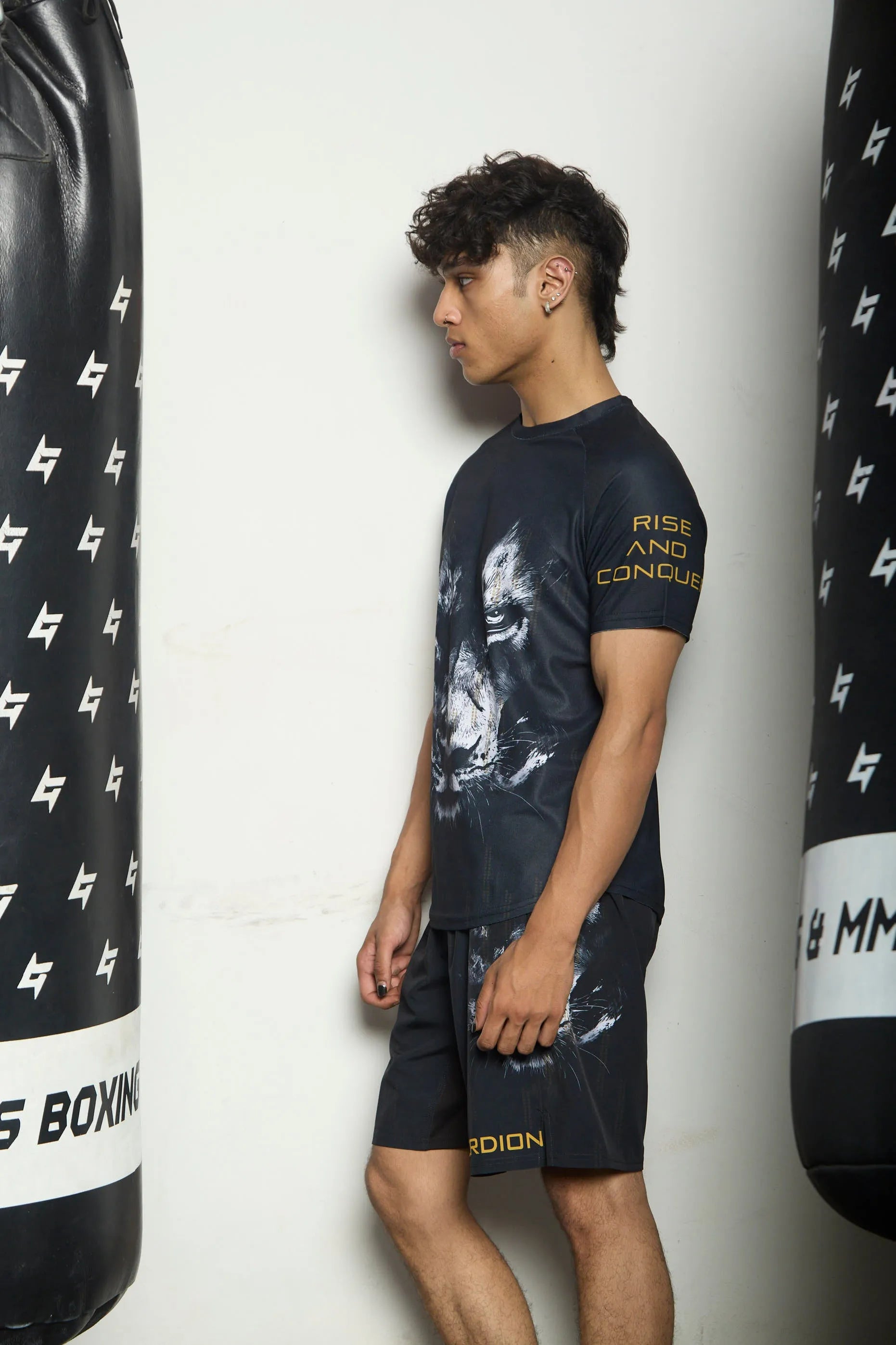 Person wearing t-shirt and shorts with boxing-themed designs, standing between two punching bags.
