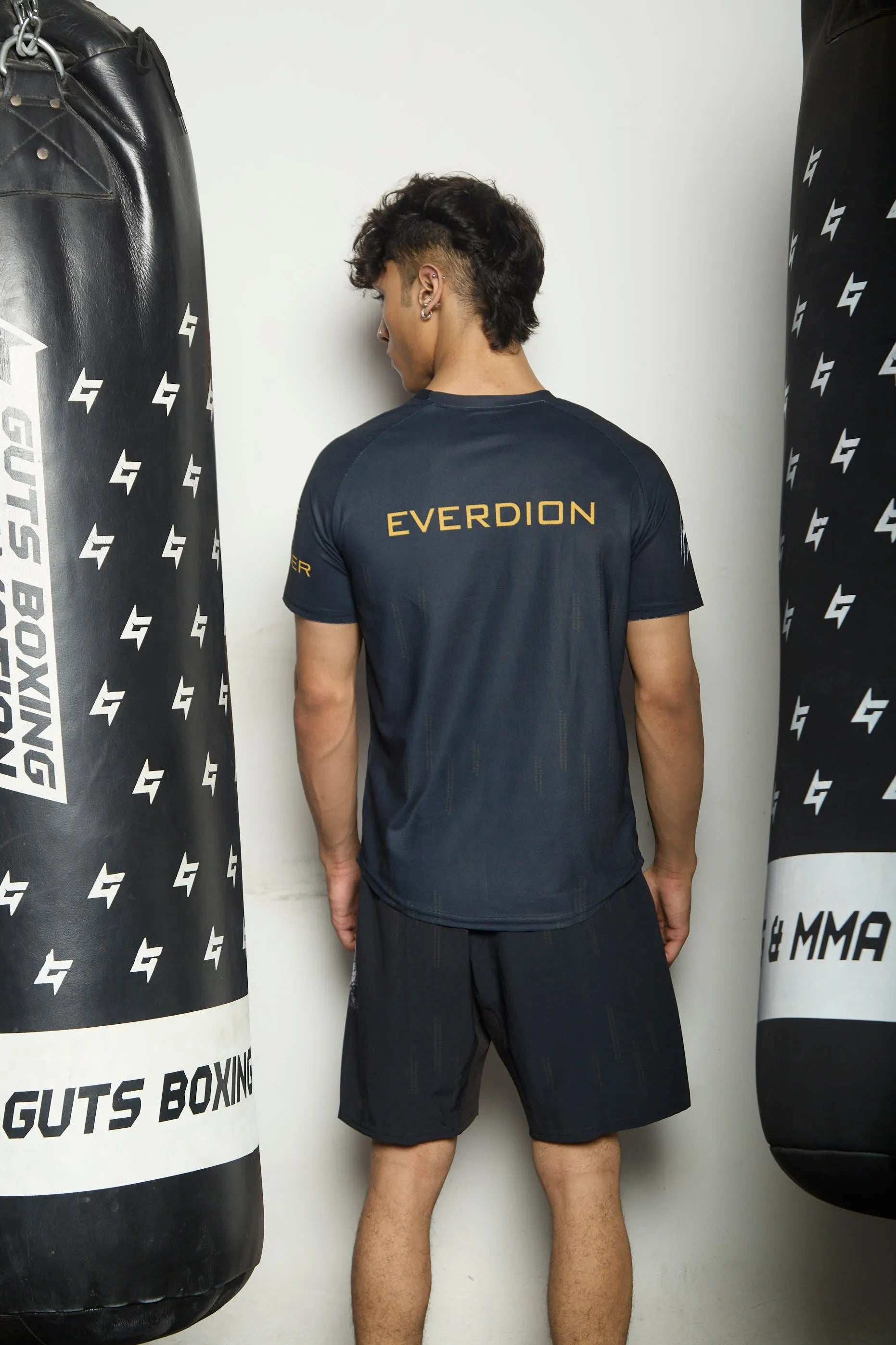 Person wearing a dark blue 'EVERDION' t-shirt and shorts standing between two punching bags with branding.