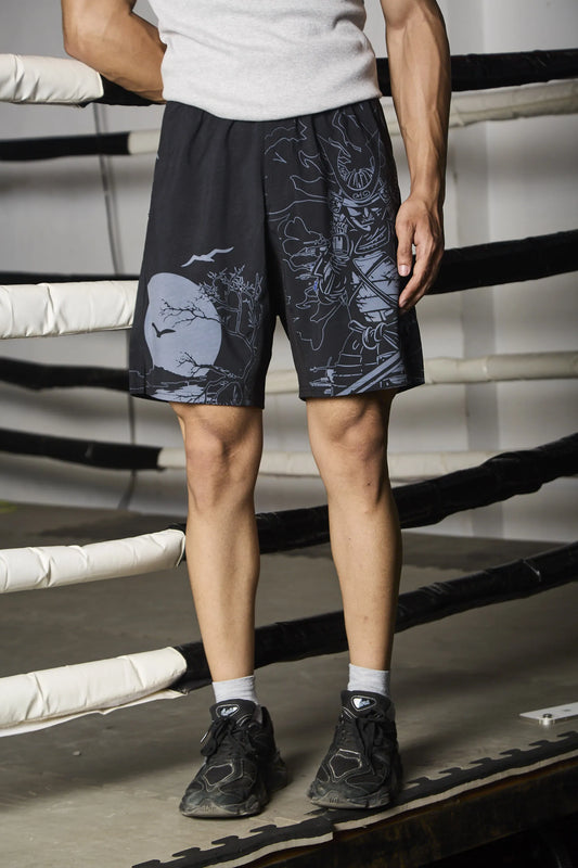 Person wearing black shorts with a graphic design standing in a boxing ring.