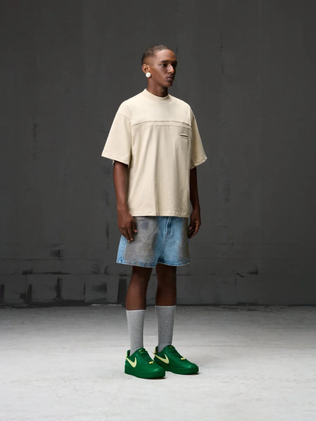 Person wearing a beige t-shirt, blue shorts, and green shoes against a grey background