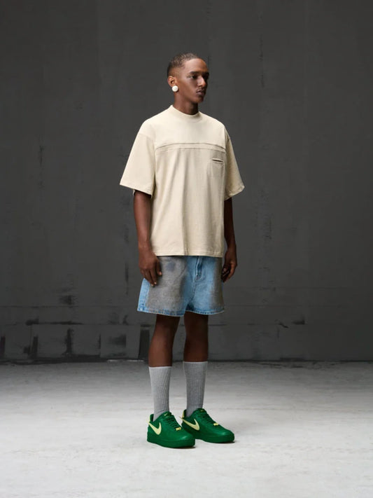 Person wearing a beige t-shirt, blue shorts, and green shoes against a grey background