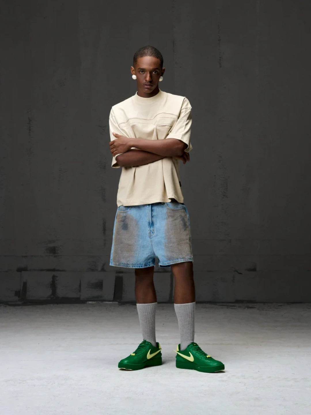 Person wearing a beige t-shirt, denim shorts, and green sneakers against a dark background