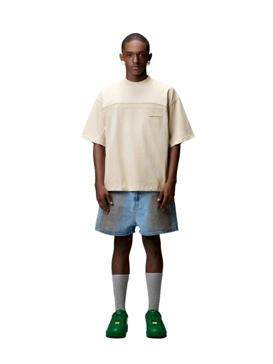 Person wearing a beige t-shirt, blue shorts, and green shoes on a white background
