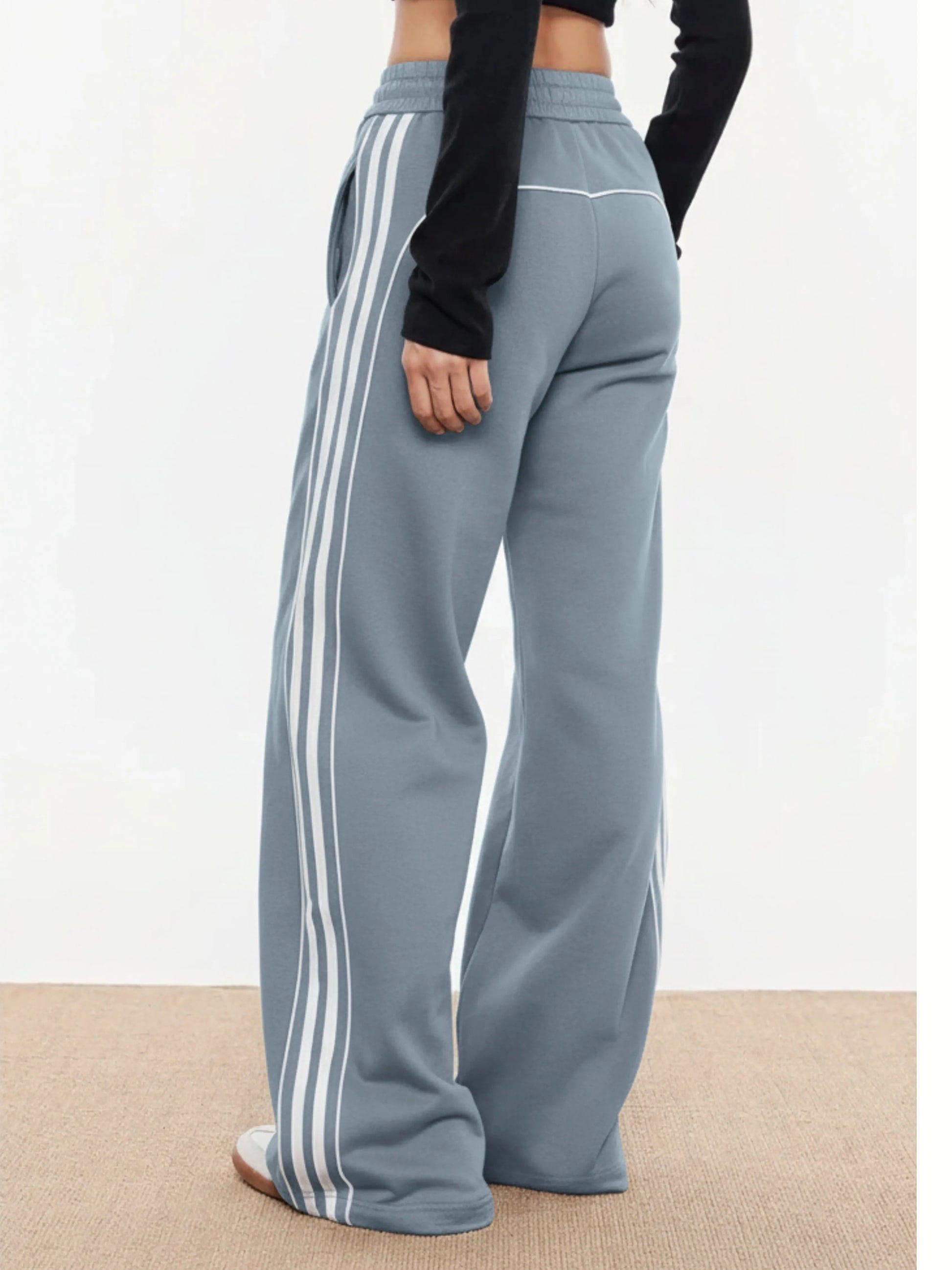Light blue trackpants with white stripes worn by a person on a plain background