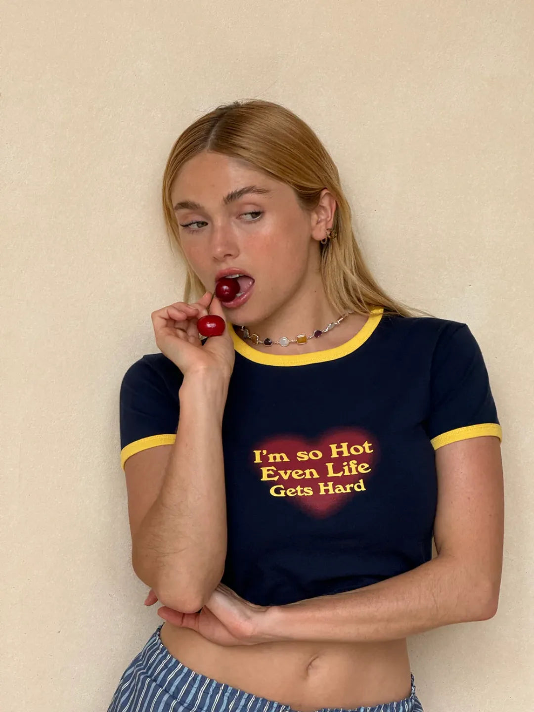 Person wearing a navy blue t-shirt with red text, holding a cherry against a beige background