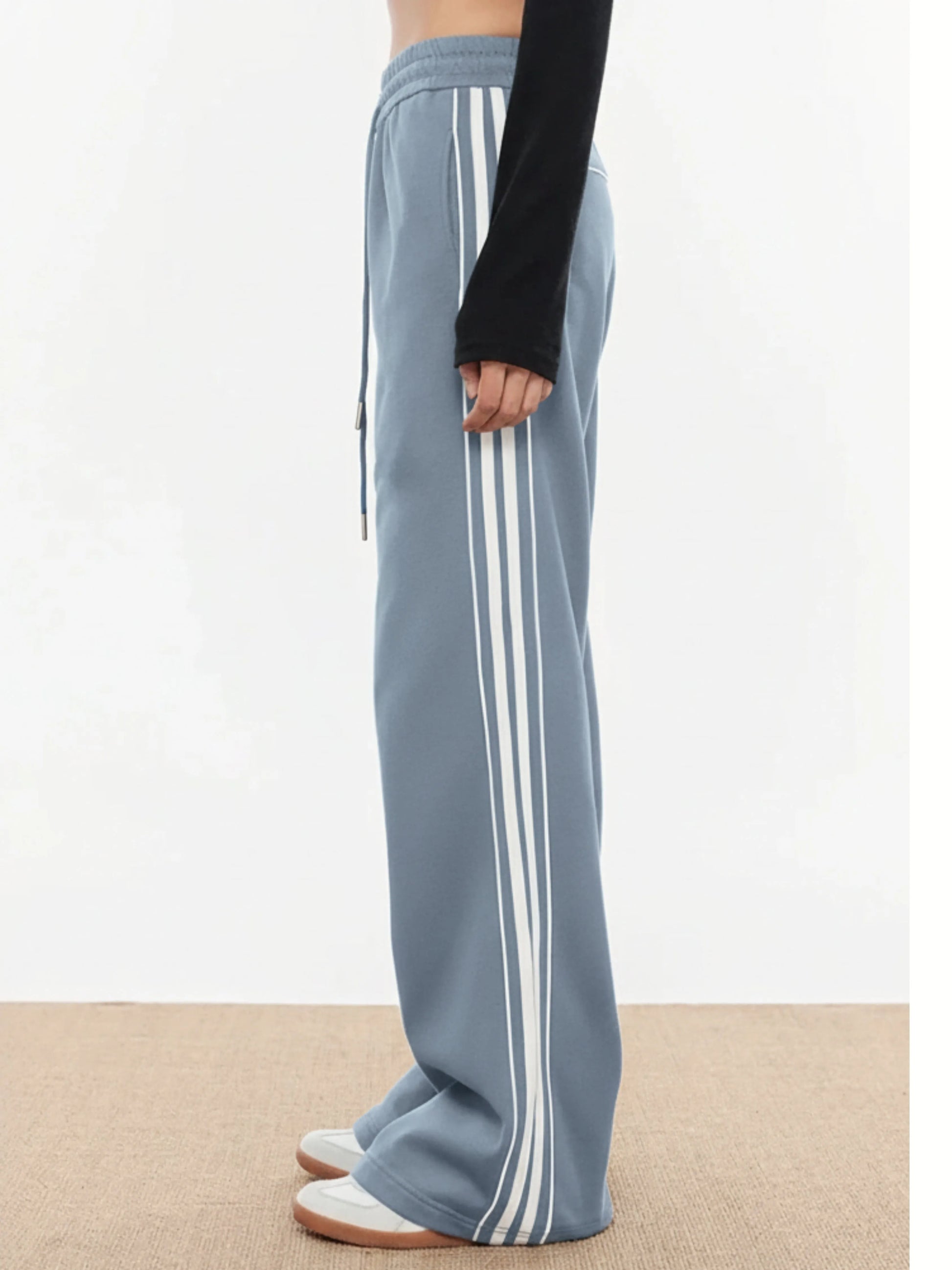 Light blue track pants with white stripes worn by a person on a neutral background