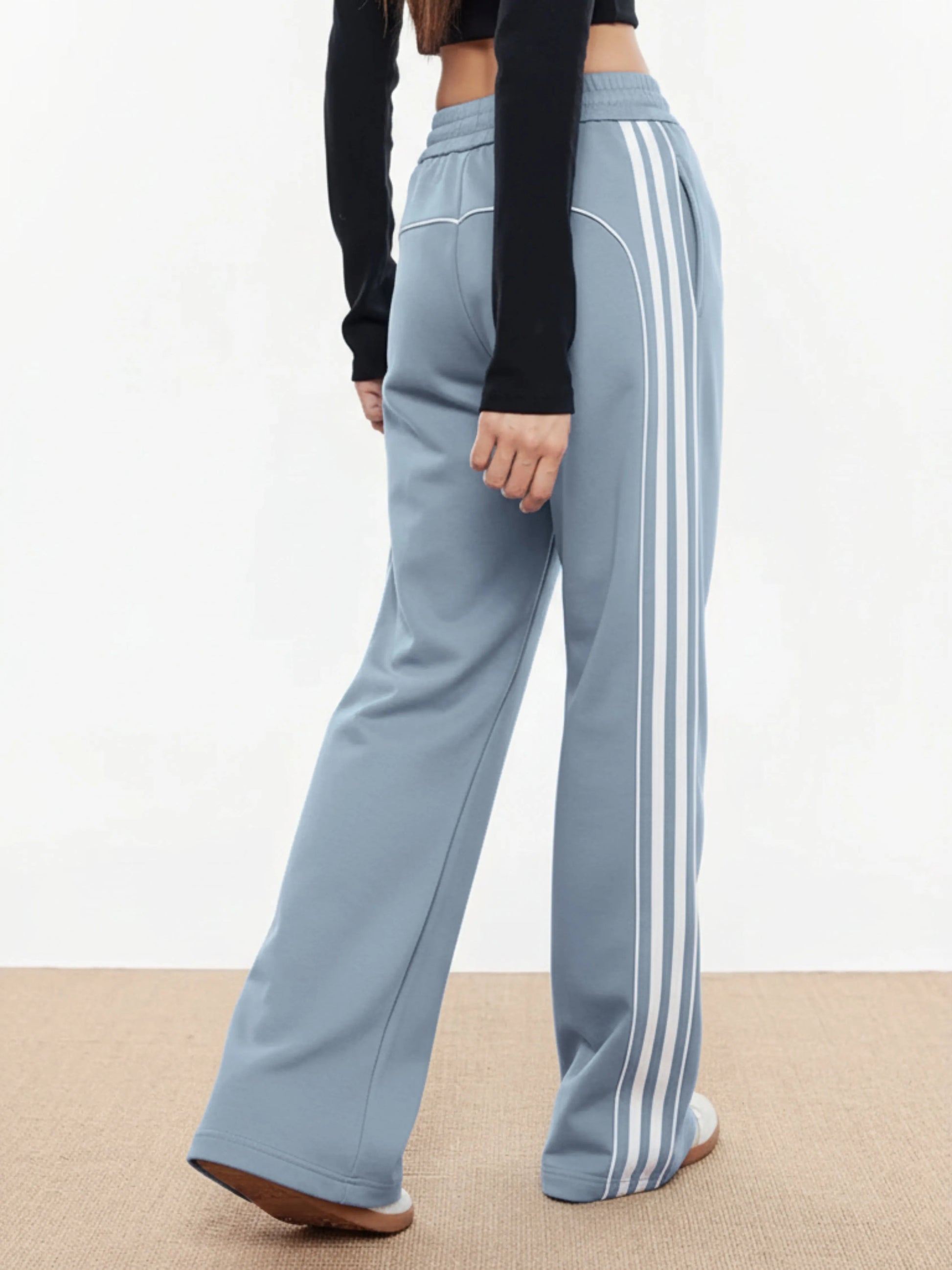 Light blue trackpants with white stripes worn by a person on a beige floor.
