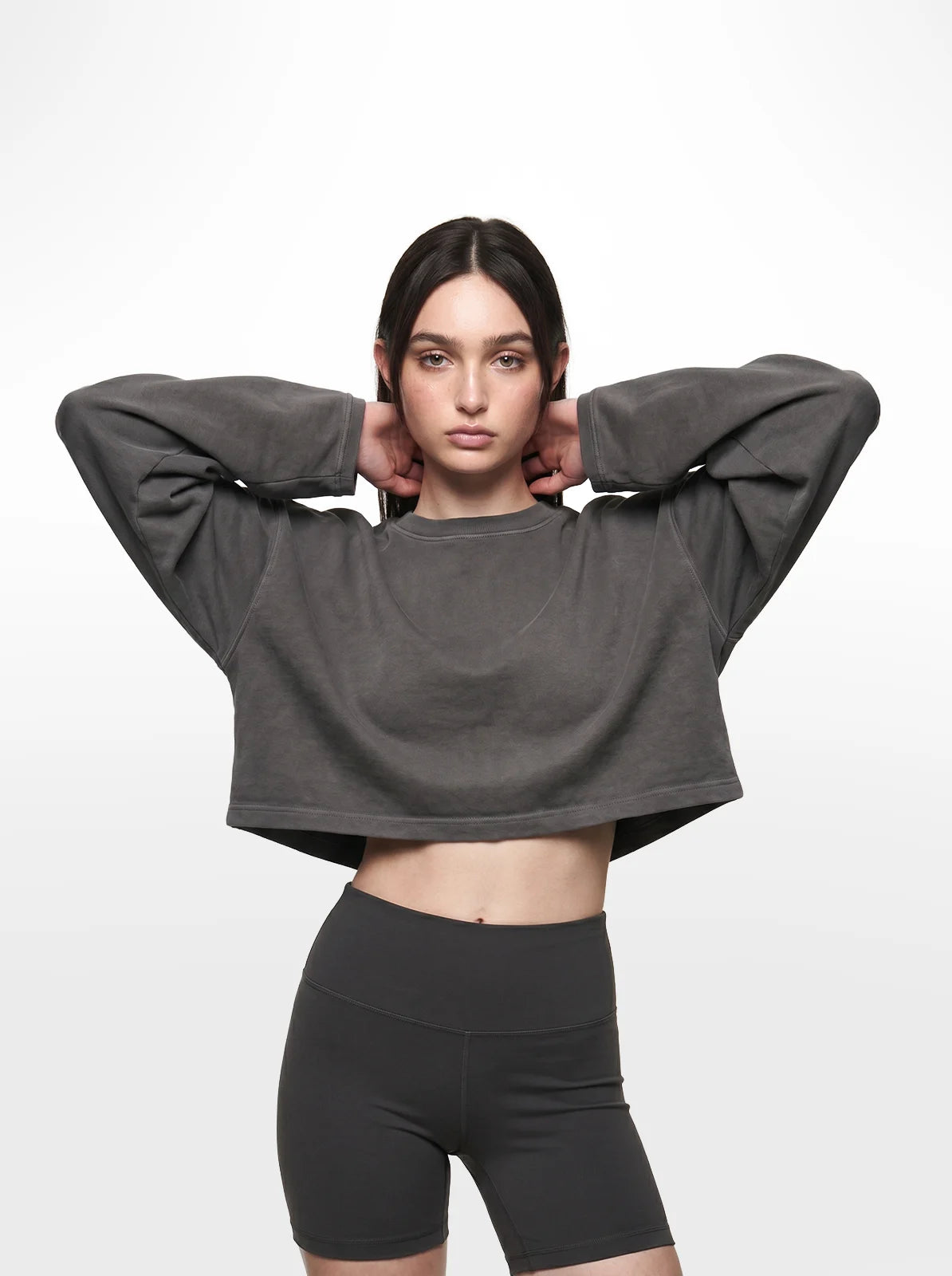 Woman wearing a grey cropped t-shirt and black shorts on a white background