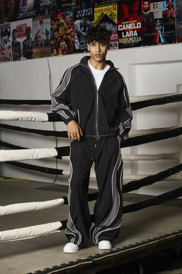 Person wearing a black tracksuit with white stripes in a boxing ring setting.