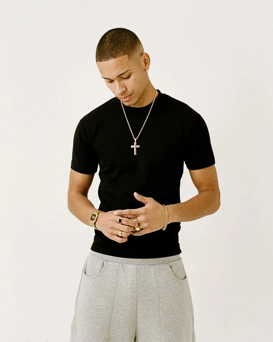 Man wearing a black fitted t-shirt and grey pants with a plain background
