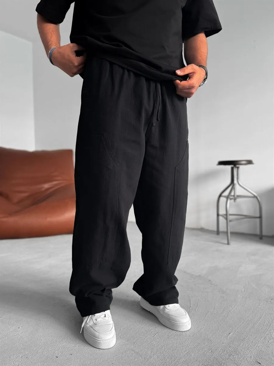 Person wearing black linen pants and a black shirt in a minimal indoor setting.