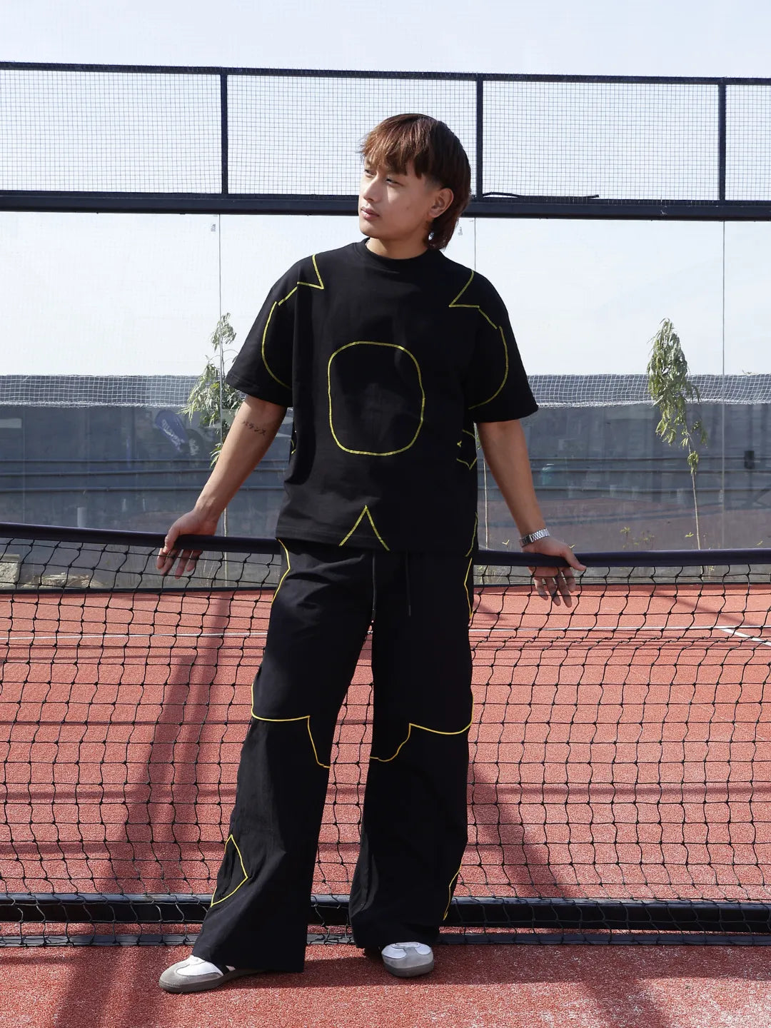 Person wearing a black outfit with yellow accents on a tennis court
