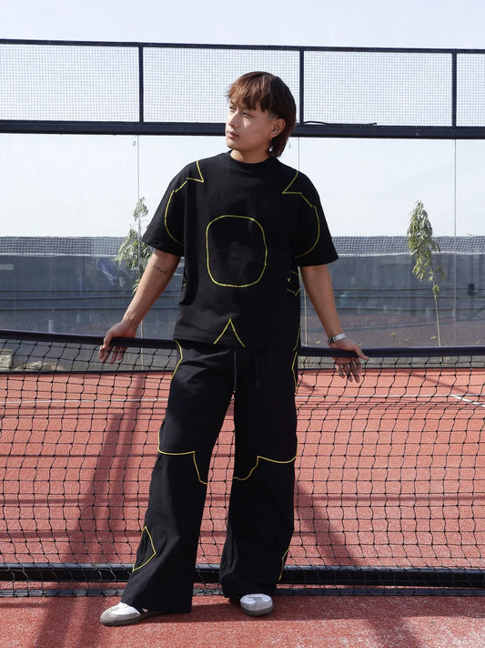 Person wearing a black outfit with yellow accents on a tennis court