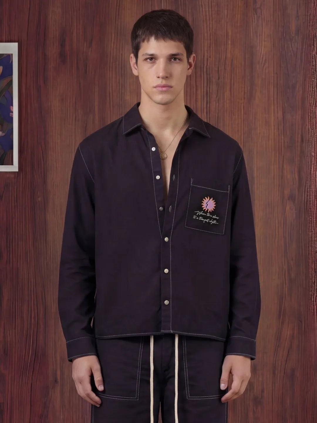 Man wearing a black shirt with a pocket patch against a wooden wall