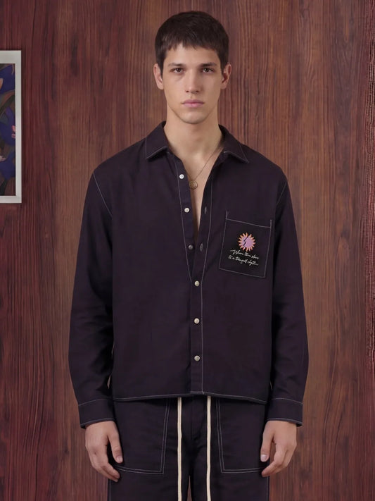 Man wearing a black shirt with a pocket patch against a wooden wall