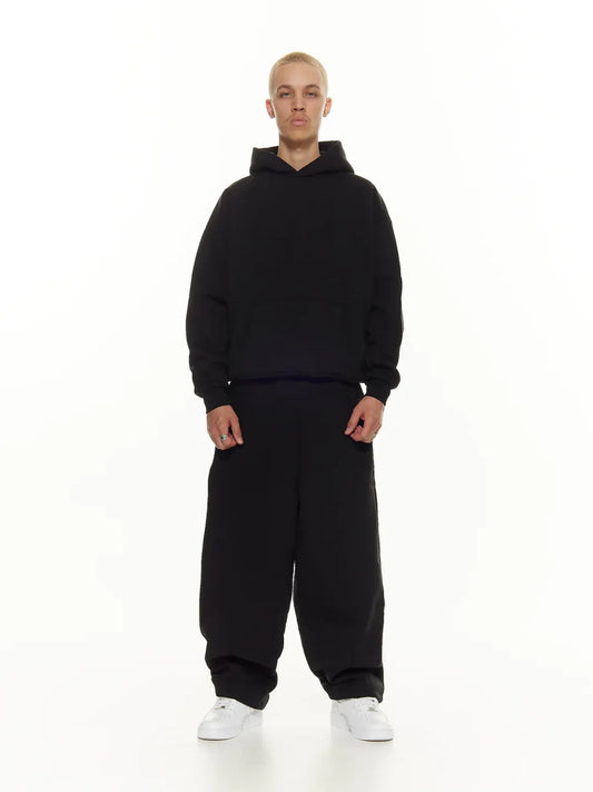 Person wearing a black hoodie and pants on a white background