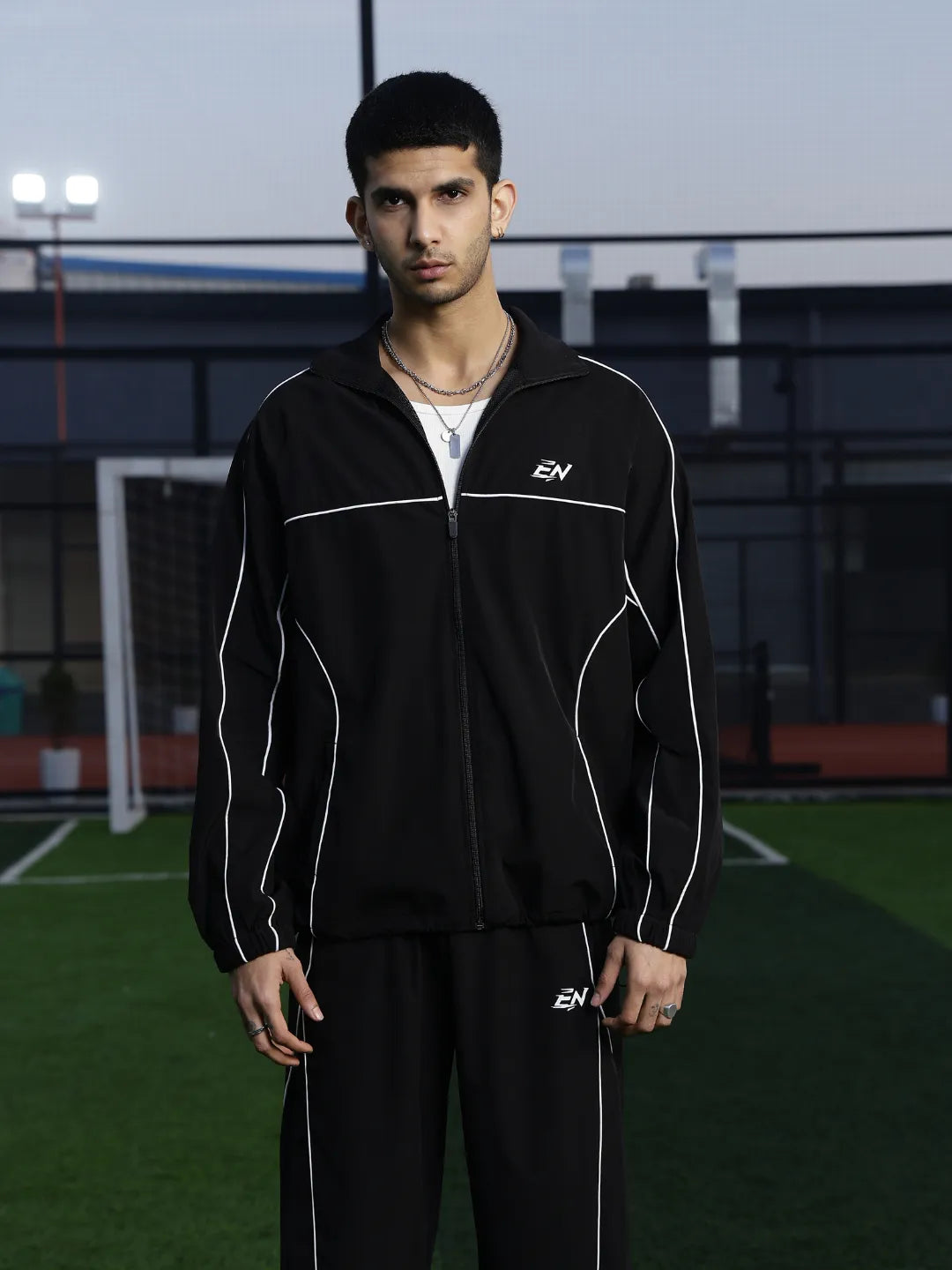 Man wearing a black tracksuit with a logo on an outdoor sports field
