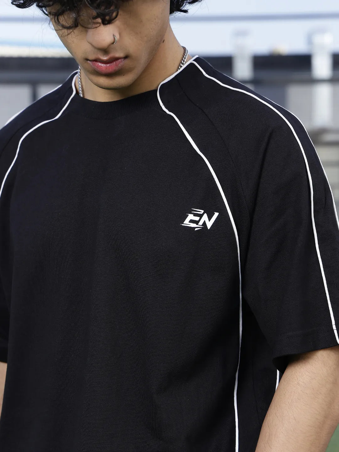 Person wearing a black sports t-shirt with a logo on it, standing indoors.