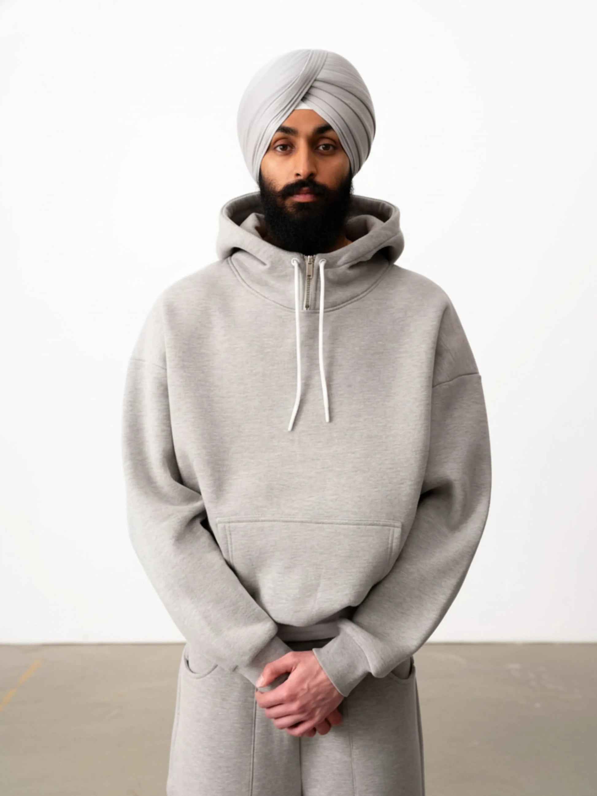 Person wearing a grey hoodie and turban against a white background
