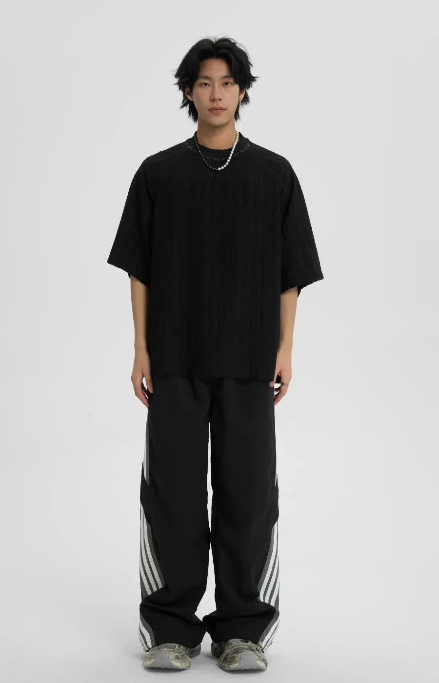 Person wearing a black oversized t-shirt and black pants with white stripes on a white background