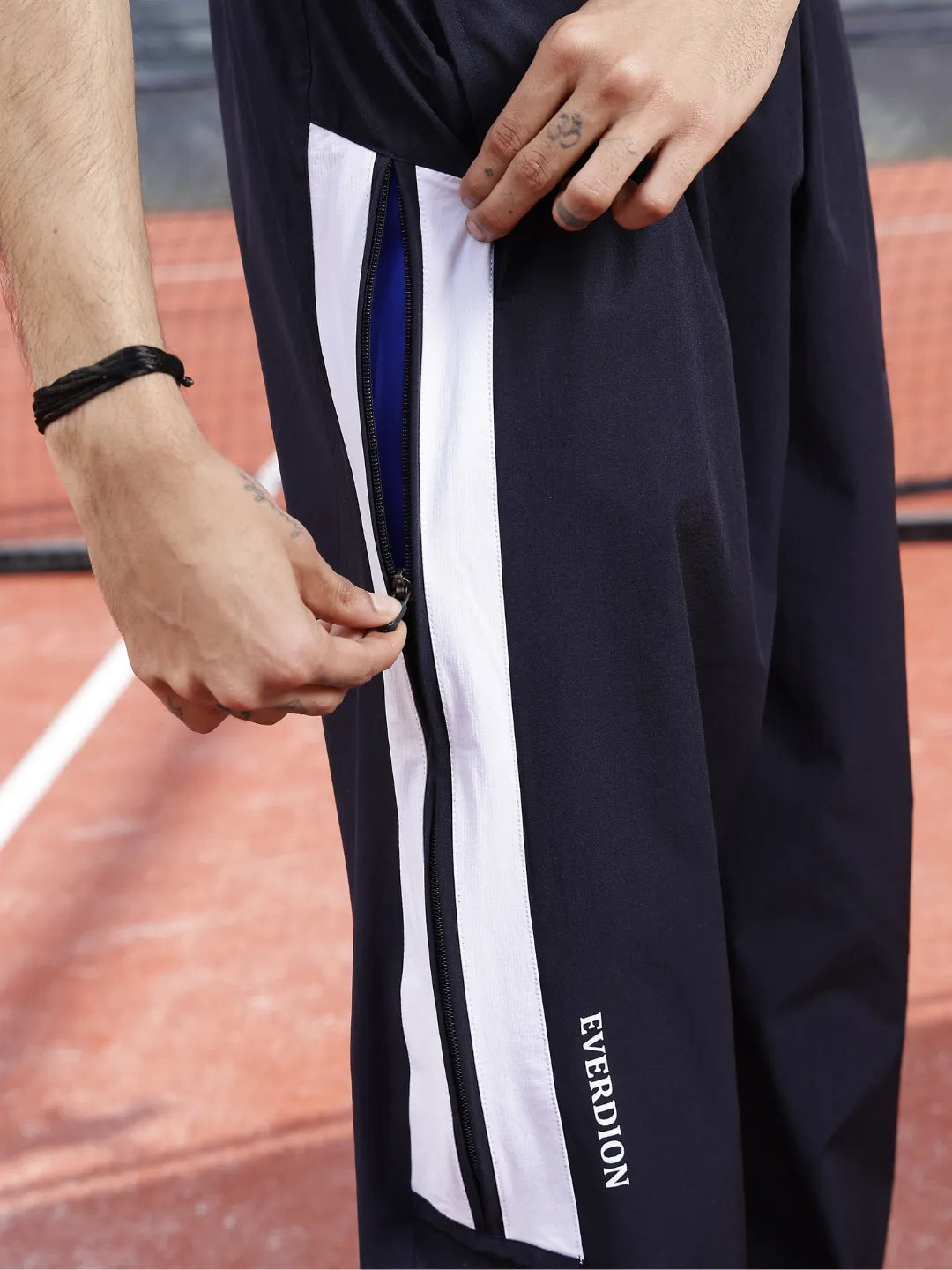 Person wearing navy blue sports pants with white stripes and 'Everdion' branding on a tennis court.