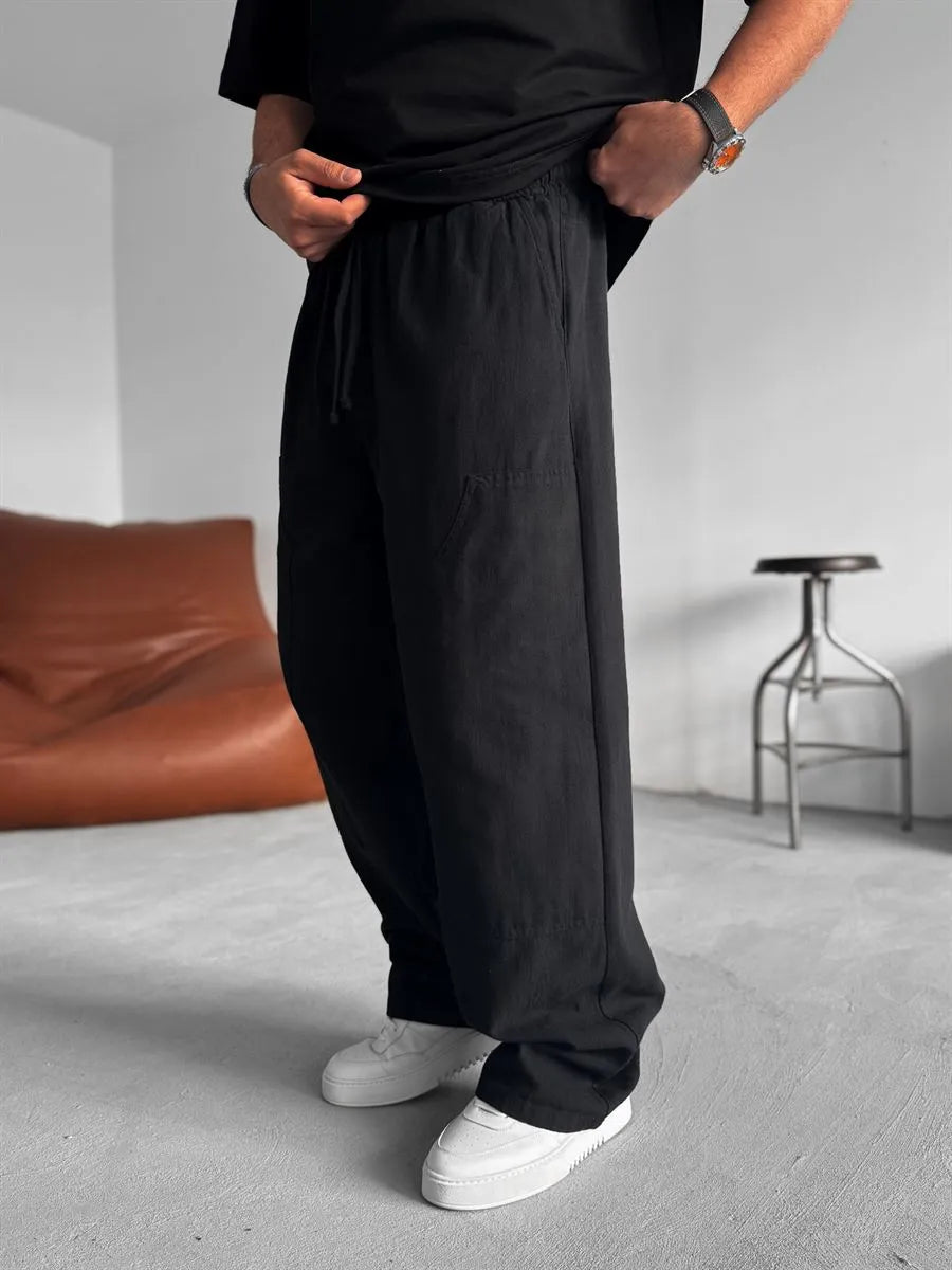 Person wearing black linen pants and white shoes in a minimal indoor setting