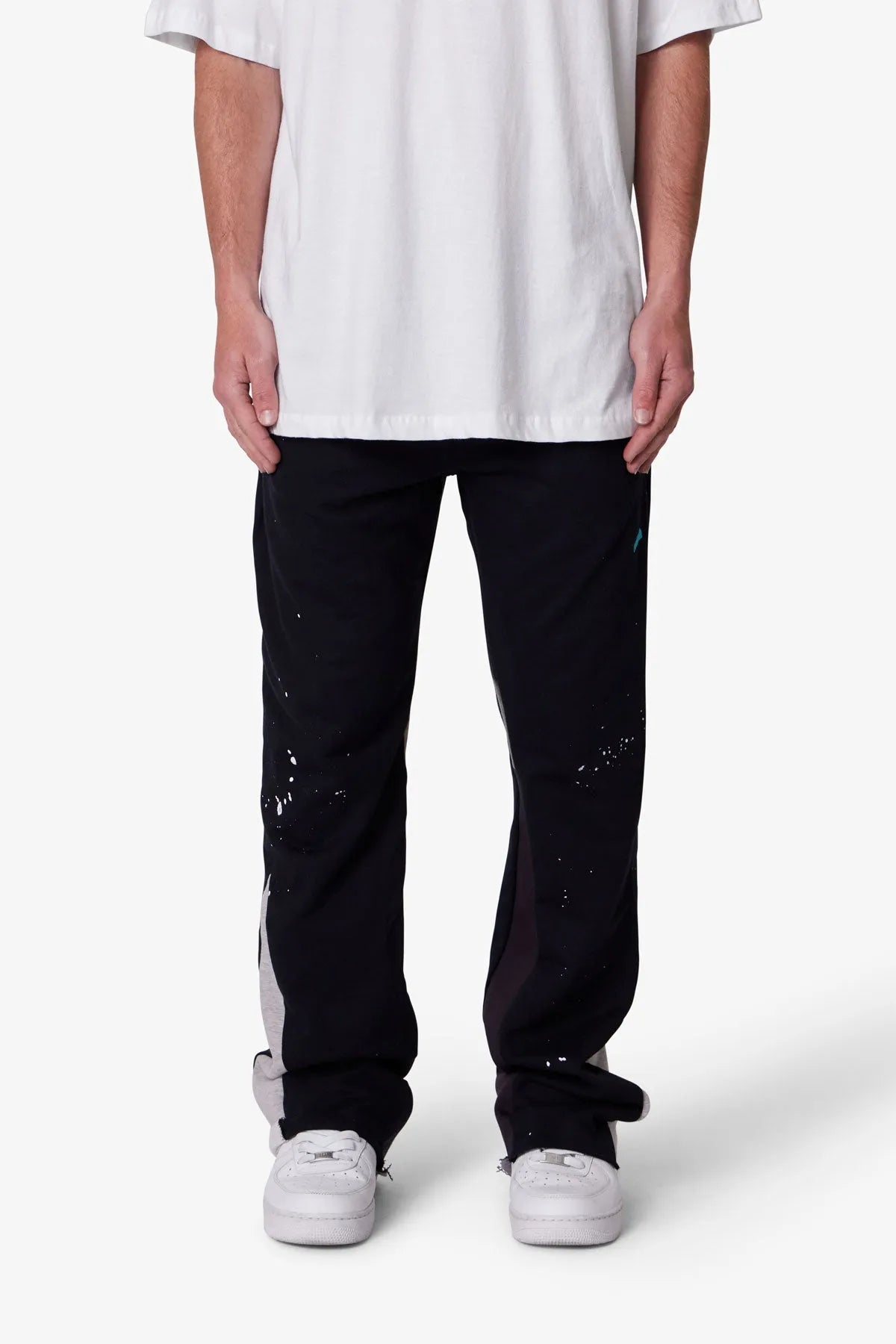 Person wearing black pants with white splatter design and a white shirt on a white background